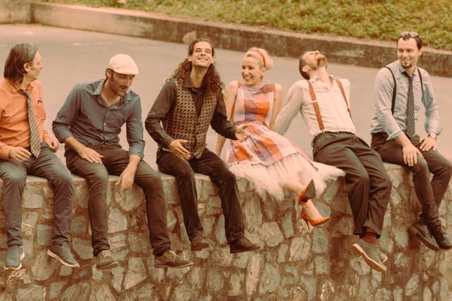The band sitting on a low stone wall, laughing