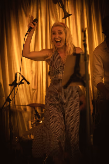 The singer with her arms spread wide in front of a gold curtain