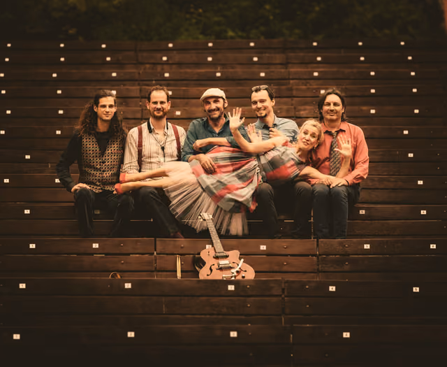 The band sitting on wooden steps under a string of lights