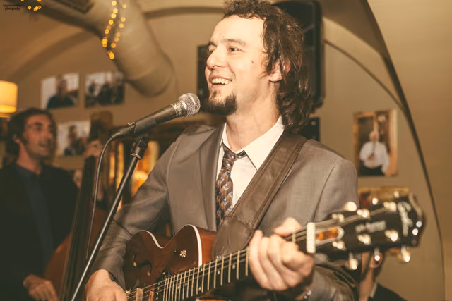 The guitarist singing at the microphone and playing in a vaulted tavern