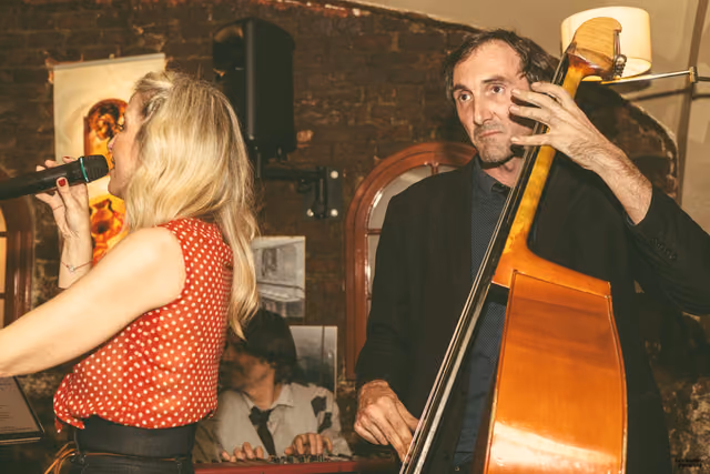 The singer at the microphone with a double bass player beside her, in a brick tavern