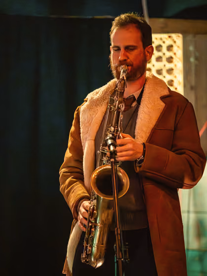 The saxophonist in a long coat with a fur collar, playing
