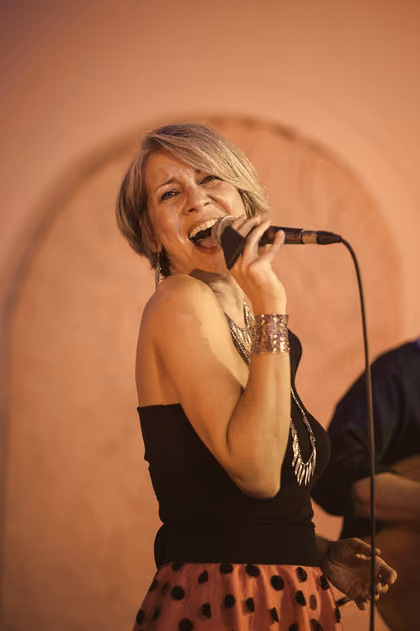 The singer smiling at the microphone in front of a pink wall